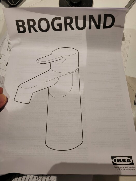 En hand håller ett IKEA-instruktionsblad för BROGRUND, skiss av en kran, svartvit.