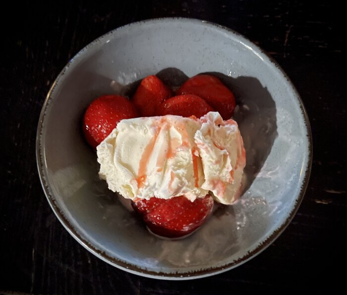 Skål med jordgubbar och vispgrädde, mörk bakgrund. Dessert eller mellanmål, fräsch, somrig, enkel.