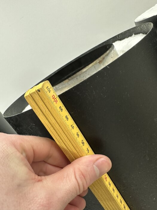 En person mäter dimension på svart föremål med en gul tumstock.