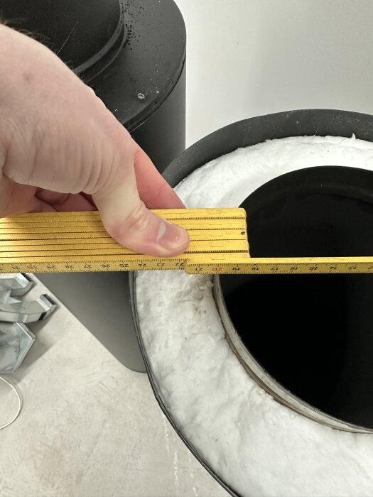 Mätning av soptunnans öppning med metallått, vita handskar och svart lock.