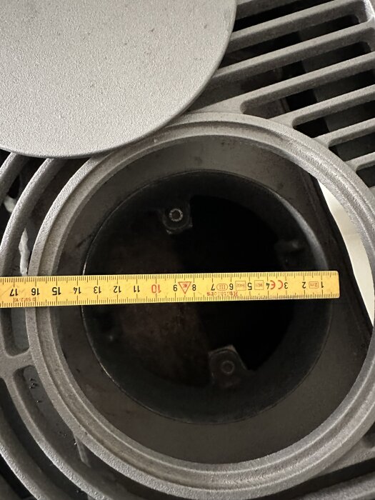 Mätverktyg (tumstock) ligger tvärs över mörk rund öppning, grått industriellt objekt, närbild, konstruktionselement.