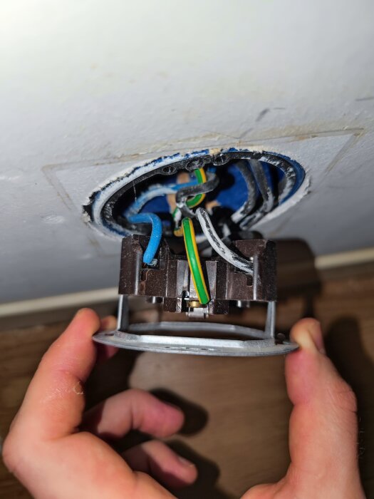 Öppen eluttag, trådar anslutna, oavslutad installation, säkerhetsrisk, person som håller en del.