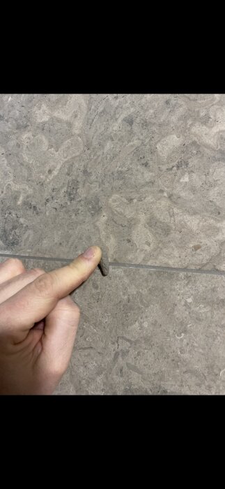 En hand pekar på en spricka i en stengolvplatta.