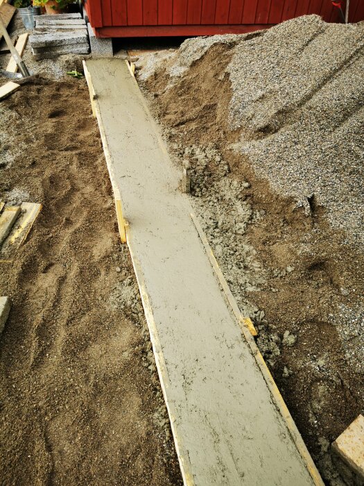 Ny betonggång gjuts, omgiven av sand och grus, vid byggarbetsplats.