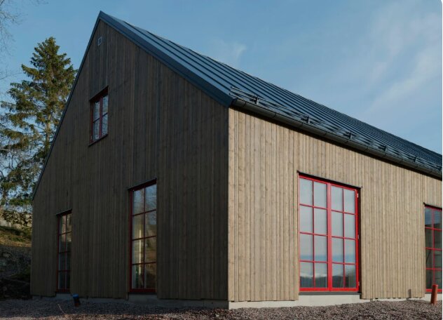 Träbeklädd byggnad, röda fönsterramar, skiffergrått tak, modernt, minimalistiskt, arkitektur, delvis molnig himmel.