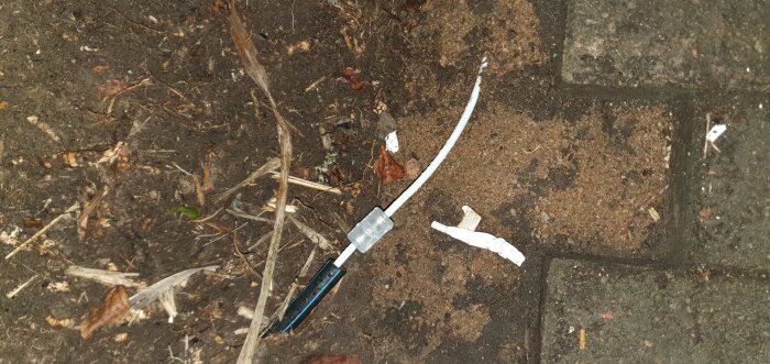 Trasig USB-laddningskabel på trottoarsten och smutsig mark. Nedskräpning, slitage, elektronikavfall, utomhus.