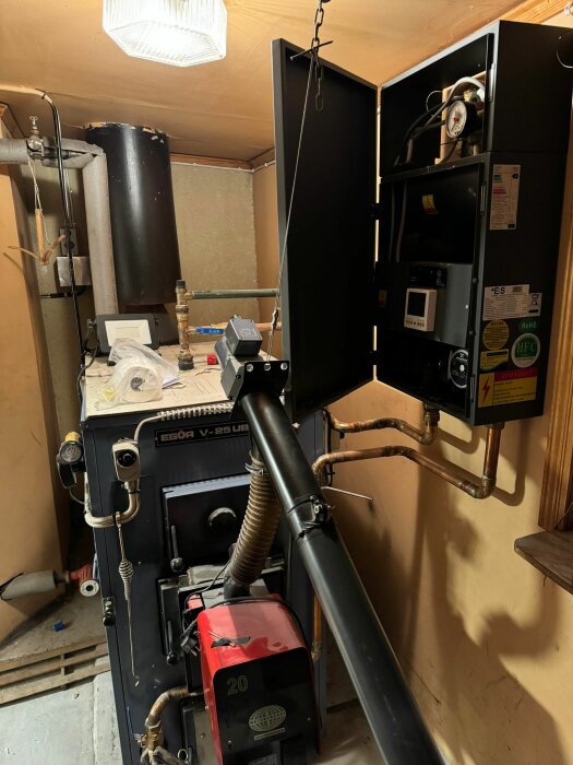 Vedeldad panna och ackumulatortank i ett pannrum med diverse teknisk utrustning och rörinstallationer.