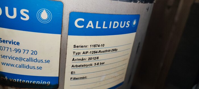 Etikett med teknisk information, kontaktuppgifter, blå och vit. "CALLIDUS", serienummer, typ, årtal, arbetstryck, filtermaterial.