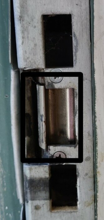 Dörrlåsets mekanism, nedslitet silverfärgat metallskena, delvis inzoomad, svart bakgrund.