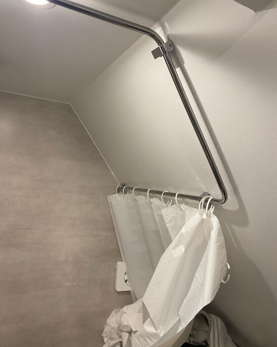 Kromad duschstång, vit duschdraperi delvis på golvet, neutral badrumsinredning.