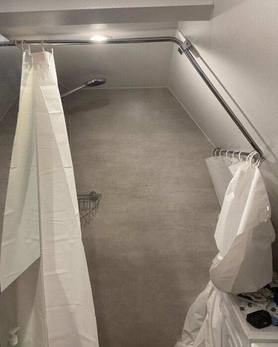Inuti ett tomt, modernt duschutrymme med öppna vita duschdraperier och kakelklädda väggar.