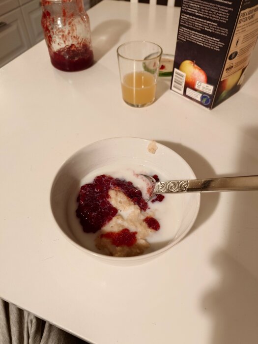 Havregrynsgröt med sylt och mjölk, juiceglas, syltburk och mjölkförpackning på bord.