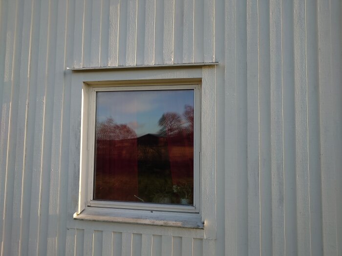 Vit metallvägg med fönster, reflekterande träd, blå himmel, utomhus, dagtid.