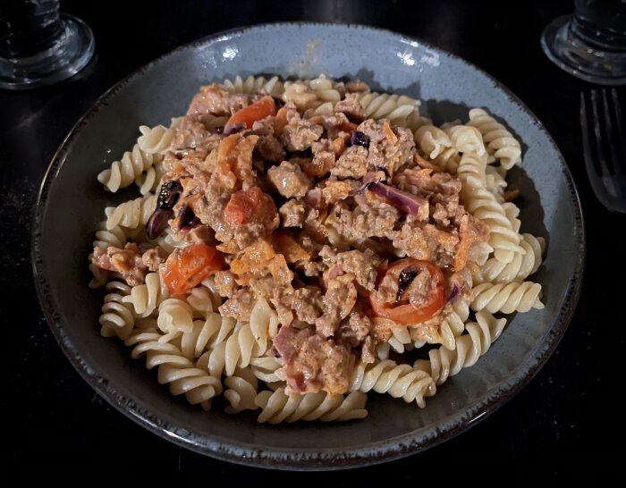 Ett fat med pasta och köttsås med tomat och lök, serverad på mörk tallrik.