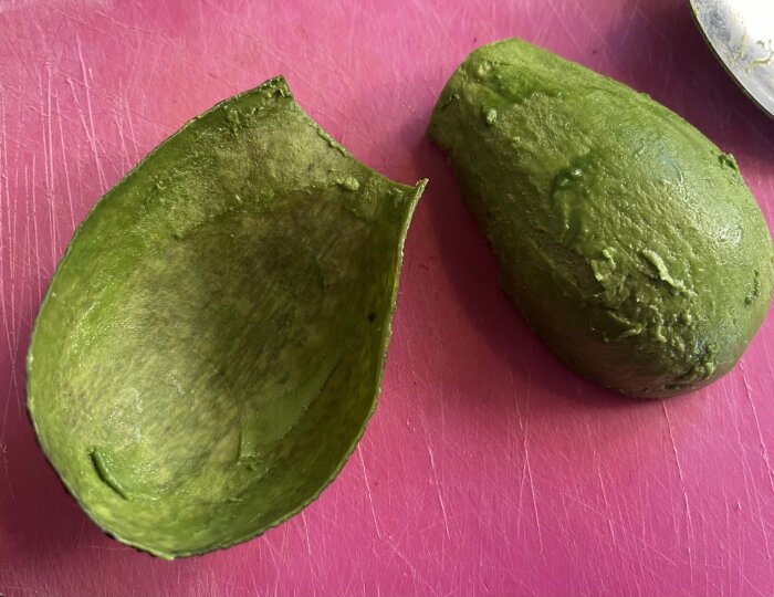 En halverad, urgröpt avocado på en rosa skärbräda. Fresh, mogen, grönskande, hälsosam, klar för att ätas eller användas i recept.