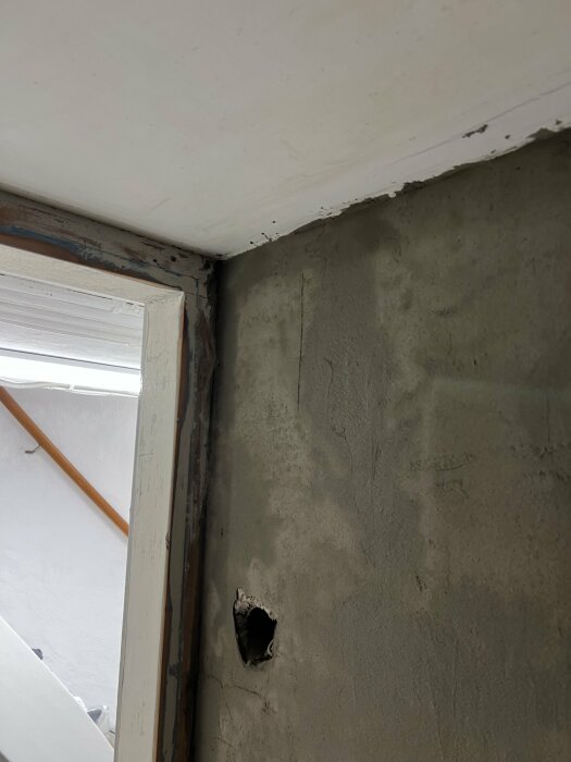 Hörnet av ett rum med sprucket tak, sliten fönsterkarm och hål i betongväggen.