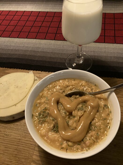 En skål med gröt och ett hjärtformat pålägg, skiva ost, glas mjölk, rutig bordstablett.