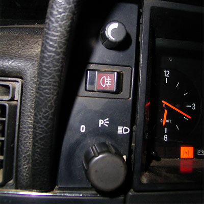 Bilinstrumentpanel närbild: ratt, kontrollknappar, parkeringsljus symbol, bränslemätare, varvräknare, röd indikator.