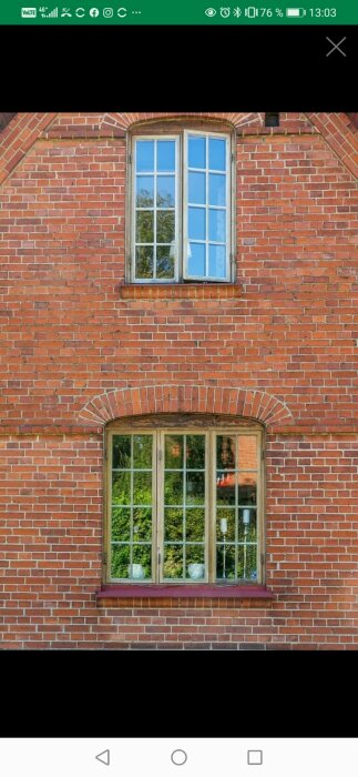 Rött tegelhus med två fönster, träd reflekteras i nedre fönstrets glas.