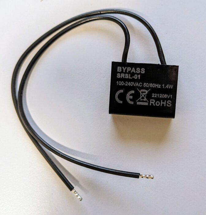 Svart bypass-modul med kablar, märkt 100-240VAC, CE, och RoHS. Ligger på ett vitt underlag.
