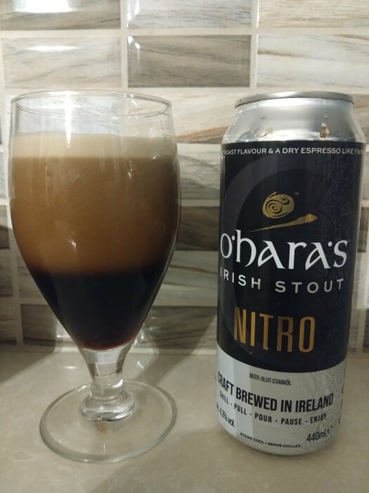 Ett glas mörkt öl brevid en burk stout. Skummande topp. "Brewed in Ireland" synligt på burken.