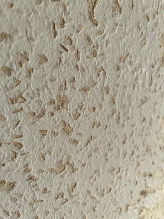 Strukturerad vit väggyta med oregelbundna, upphöjda bruna fläckar. Dekorativ stuckatur eller målning, närbild.