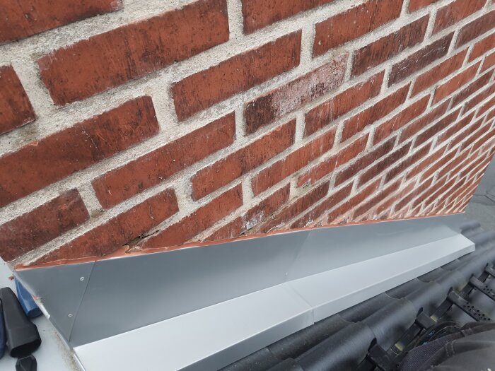 Tegelvägg med mörtel, silverfärgad metallavsats eller fönsterbleck, oskarp förgrund, potentiellt tak eller balkong.