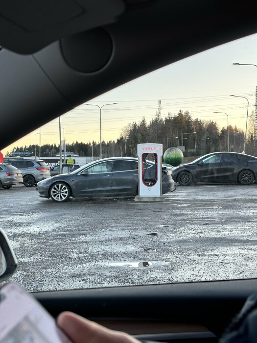 Bilden visar en Tesla-laddstation med bilar, tagen från bilens insida.