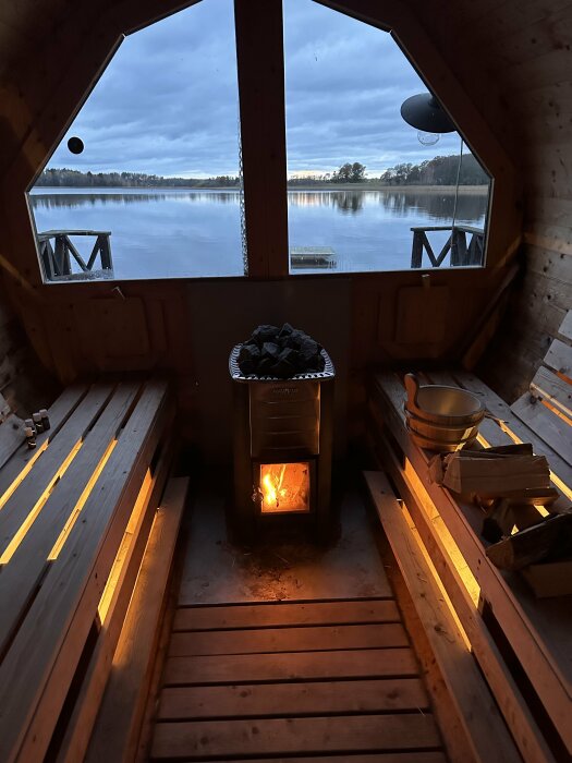 Bastu med öppen vy över sjö, brinnande kamin, träbänkar, kvällsljus, avslappnande atmosfär.