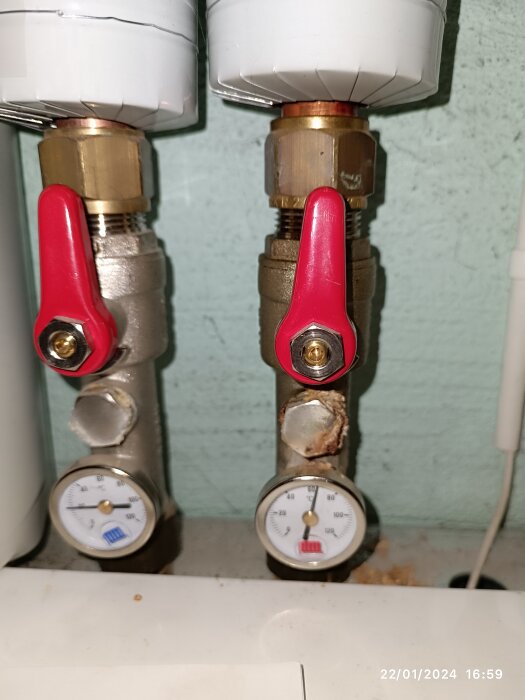 VVS-installation med röda ventiler och två manometrar på en vägg. Möjlig korrosion eller läckage synlig.