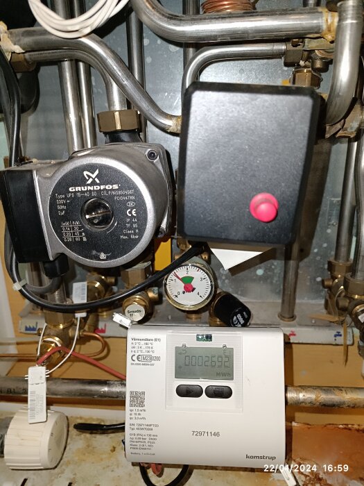 Värmeinstallation med cirkulationspump, rör, mätinstrument och värmemätare i ett teknikutrymme.