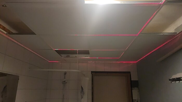 Nedmonterat taktak med synliga reglar, rosa LED-ljus, ofärdigt rum under renovering, ljusinsläpp till vänster.