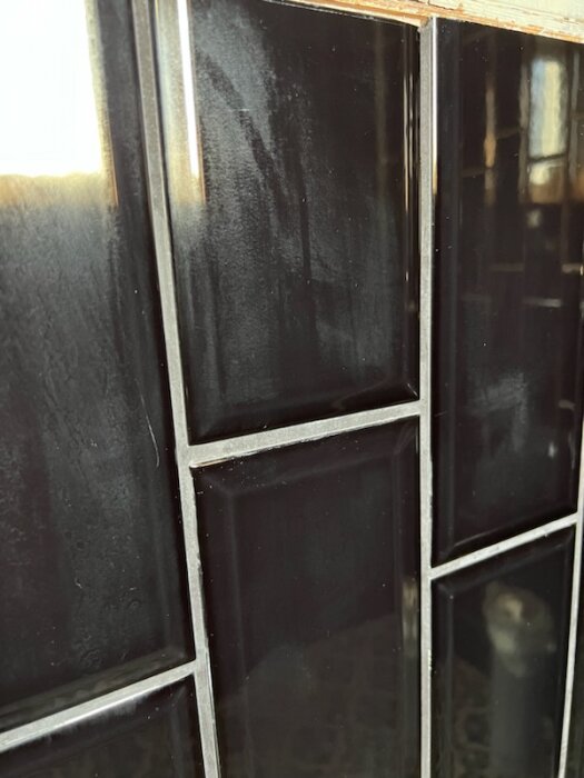 Svarta kaklade väggar med reflektioner, eventuellt i ett badrum eller kök, närbild.