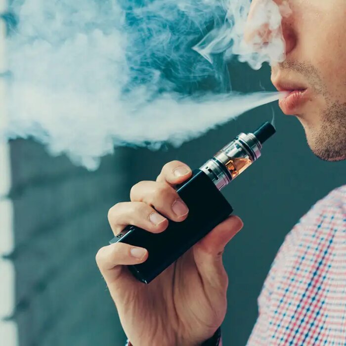 Man använder e-cigarett, blåser ut rök, närbild, utan ansiktsigenkänning, modern rökningsteknik, nikotinleveranssystem.