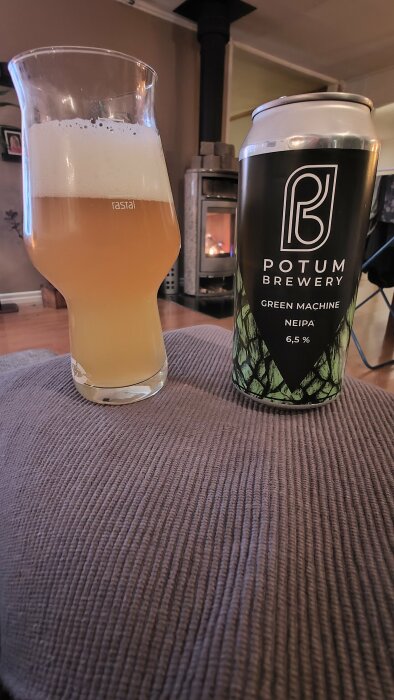 Ett glas öl bredvid en ölburk märkt "Potum Brewery Green Machine NEIPA" framför en brinnande kamin.