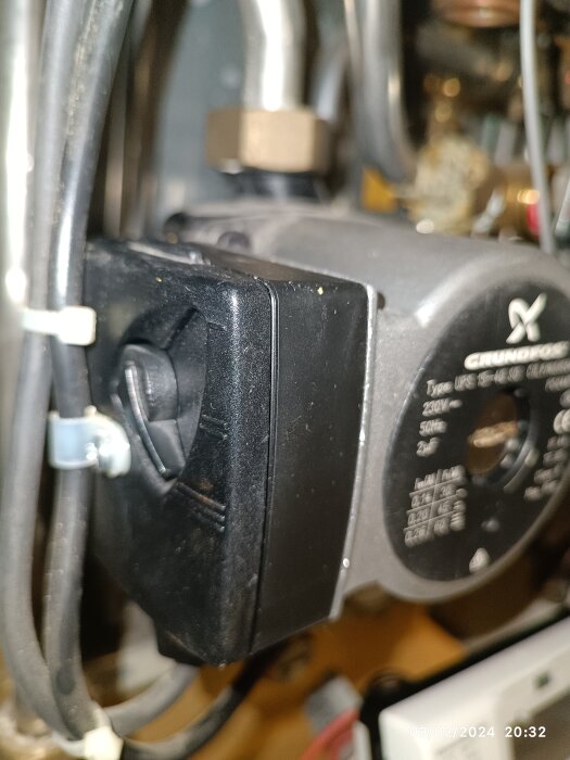 Närbild på en svart Grundfos cirkulationspump i en teknisk installation med rör och kablage.