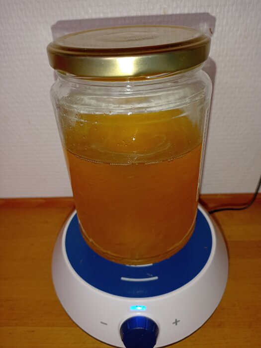 Glasburk med brun vätska på en blå uppvärmningsplatta, lysande blått ljus, guldlock, kontrollknapp i förgrunden.