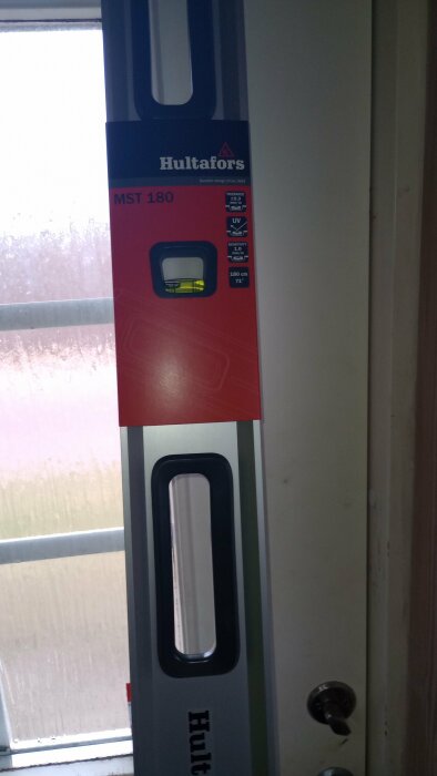 En ny Hultafors MST 180 vattenpass mot en dörrkarm, med prislapp och produktinformation synlig.