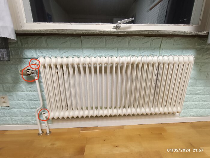 Vit radiator framför ett fönster, markerade punkter, kaklade väggar, trägolv, inomhus.