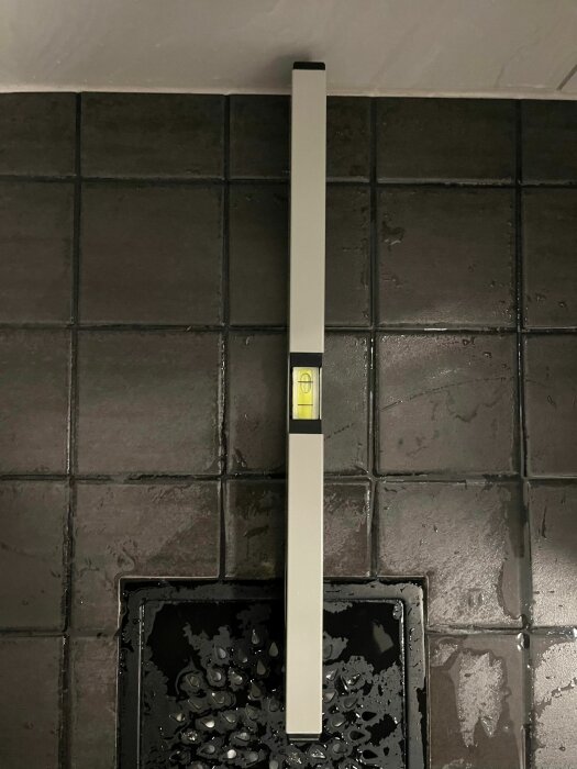 Ett vågrätt vattenpass placerat på kaklade väggen över ett våtrumsgolv med golvbrunn.