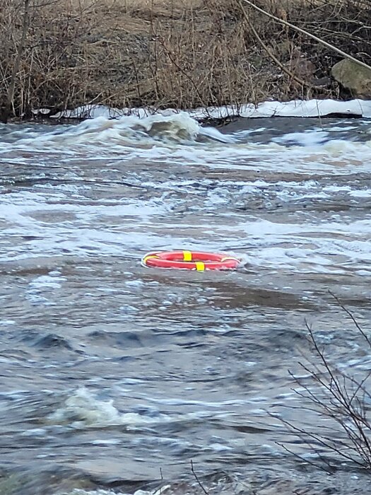 Ett rött och gult livboj flyter i ett rörigt vatten i en flod eller ström.