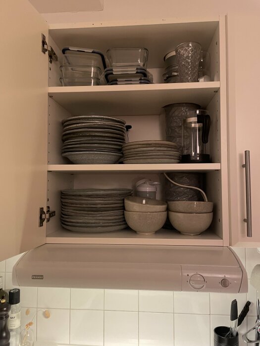 Ett köksskåp innehåller tallrikar, skålar och förvaringslådor över en mikrovågsugn, ordnat och städat.