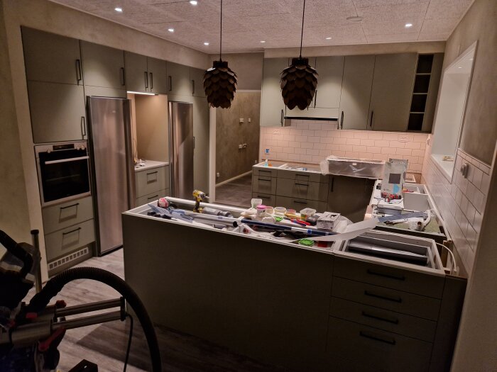 Ett kök under renovering med öppna skåp och verktyg utspridda. Modernt, halvfärdigt, rörigt.