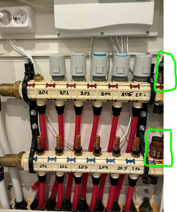 Installation för golvvärme med flera kretsar, aktuatorer och etiketterade rör. Eluttag och värmeregulator ovanför.