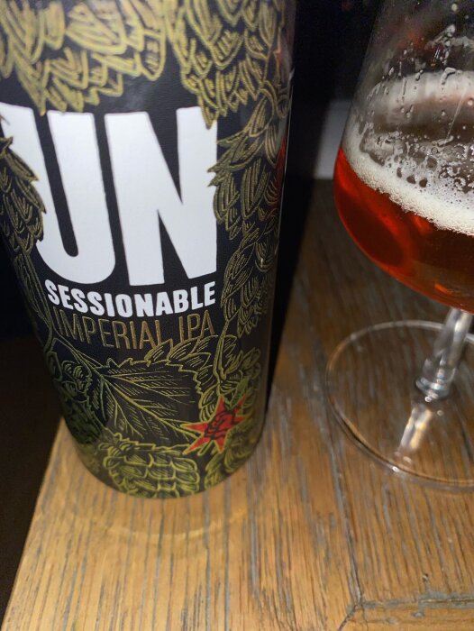 Ölburk med texten "Sessionable Imperial IPA", delvis synlig, bredvid en ölglas halvfullt, på träbord.