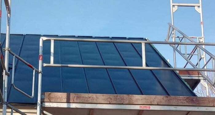 Solpaneler installerade på tak, omgivna av byggställningar, klar himmel i bakgrunden.
