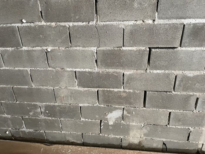 Grå tegelvägg med spricka, ojämnt murbruk, spår av slitage och fläckar.