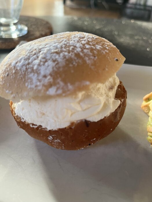 Semla med fluffig grädde mellan halverat vetebröd, pudrat med florsocker, närbild, inomhusbelysning.