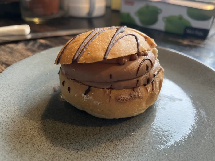 Glassburger med chokladglass och strössel, serverad på grå tallrik, bakgrund diffus köksmiljö.