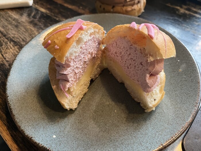 En uppskuren semla med rosa fyllning på ett keramikfat.